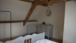 A bedroom with a white bed, wooden beams, a dresser, and a radiator.