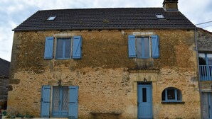 A stone building with two blue doors and windows, a small bench, and a gravel driveway.