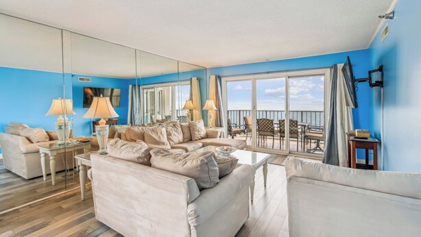 Een ruime woonkamer met een grote spiegel, beige banken, een salontafel en een balkon met uitzicht.