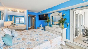 Een slaapkamer met een bed, een dressoir, een televisie en een schuifdeur die naar een balkon leidt.
