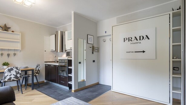 Eine moderne Wohnung mit Küche, Essbereich und Wohnzimmer. An der Wand ist ein Schild mit der Aufschrift 'PRADA MARFA 1837 MI'.