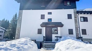 Ein zweistöckiges Gebäude mit weißer Fassade, dunklem Dach und einem zentralen Eingang mit einer Holztür.