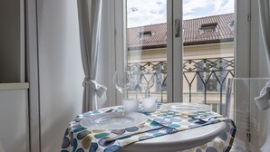 Ein Balkon mit einem Tisch für zwei Personen, ausgestattet mit einer gemusterten Tischdecke, klaren Gläsern und einem weißen Teller.