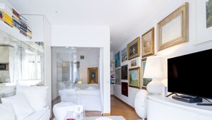Ein modernes, weißes Wohnzimmer mit einer Couch, einem Couchtisch, einem Fernseher und einer Wand mit gerahmten Bildern.