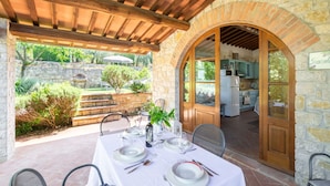 An outdoor patio with a table set for dining, stone walls, and a view of a kitchen. - Beautiful apartment in villa for 4 people with pool, A/C, WIFI, TV and pets allowed (Gaiole In Chianti)