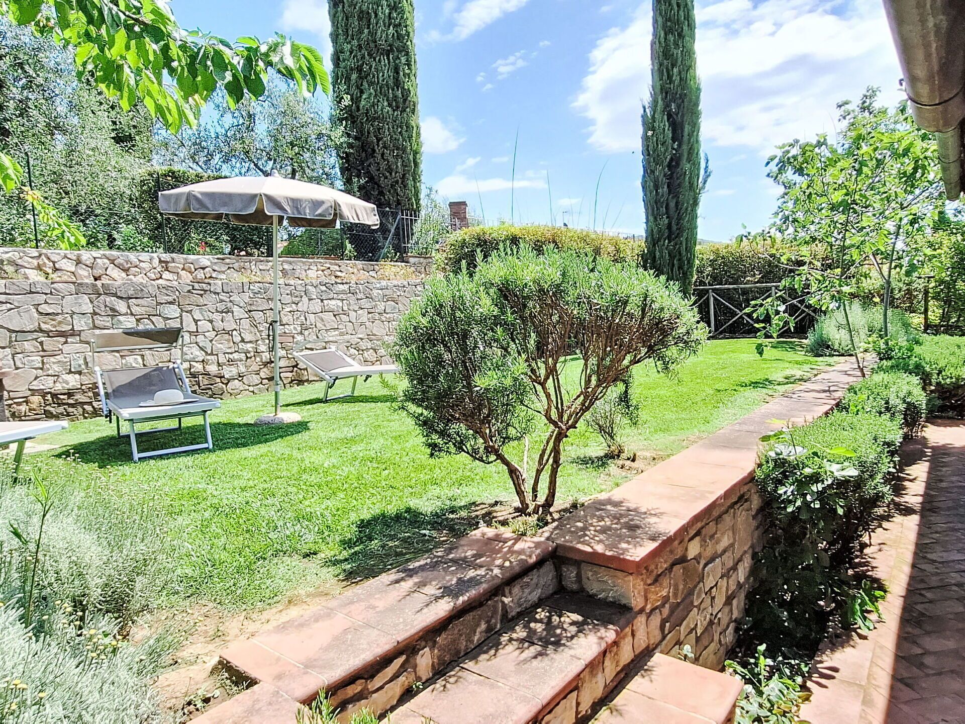 A stone wall with a small garden area, a bench, and a pergola with a canopy.