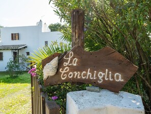 Ein rustikales Holzschild mit der Aufschrift "La Conchiglia" in einem Garten.