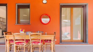 A dining area with a wooden table and chairs, a red-framed mirror, and large windows with curtains. - Nice apartment for 6 people with A/C, WIFI, TV and patio (Viareggio)