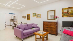 A modern living room with a purple sofa, a wooden dresser, a grey sofa, and a dining area with a table and chairs. - Nice apartment for 6 people with A/C, WIFI, TV and patio (Viareggio)