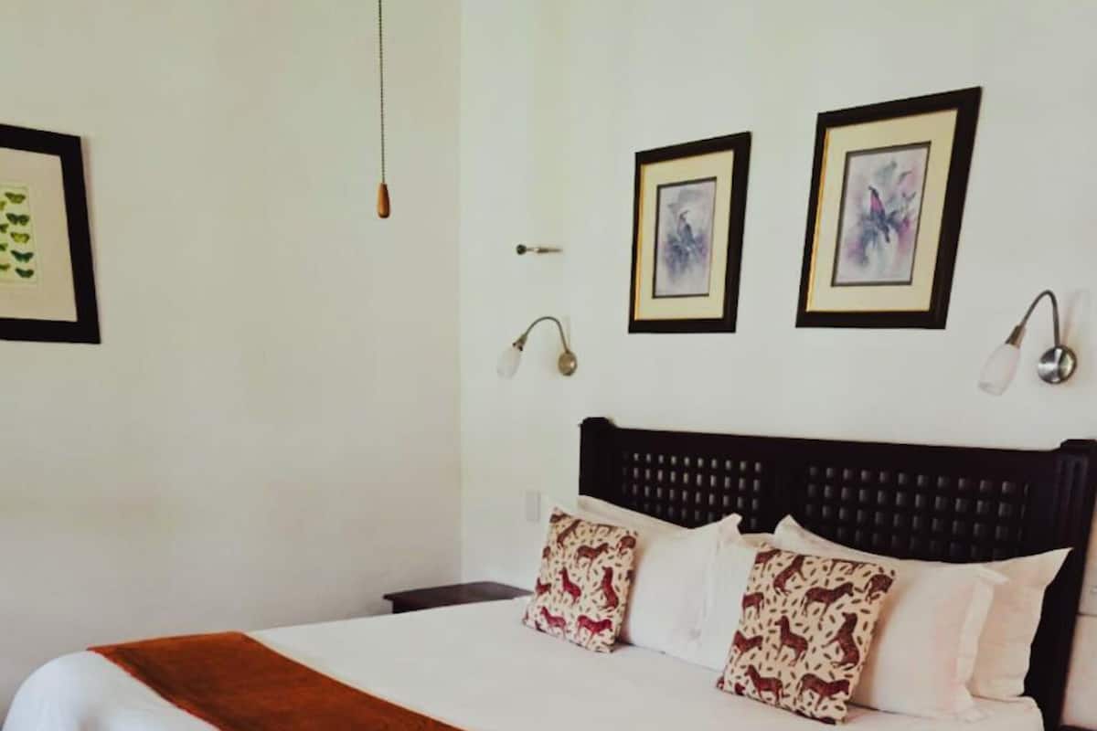 A neatly made bed with a brown blanket, white sheets, and patterned pillows. There are two wall-mounted lamps on either side of the bed.