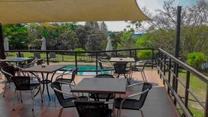 An outdoor patio area with tables and chairs, a pool, and a view of the surrounding landscape. - Kruger Island Resort (White River)