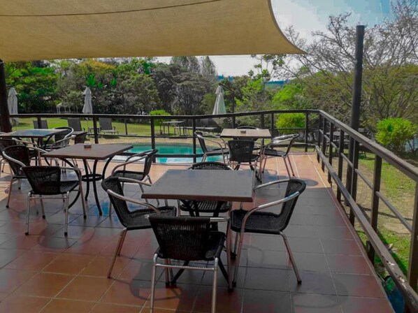 An outdoor patio area with tables and chairs, a pool, and a view of the surrounding landscape. - Kruger Island Resort (White River)