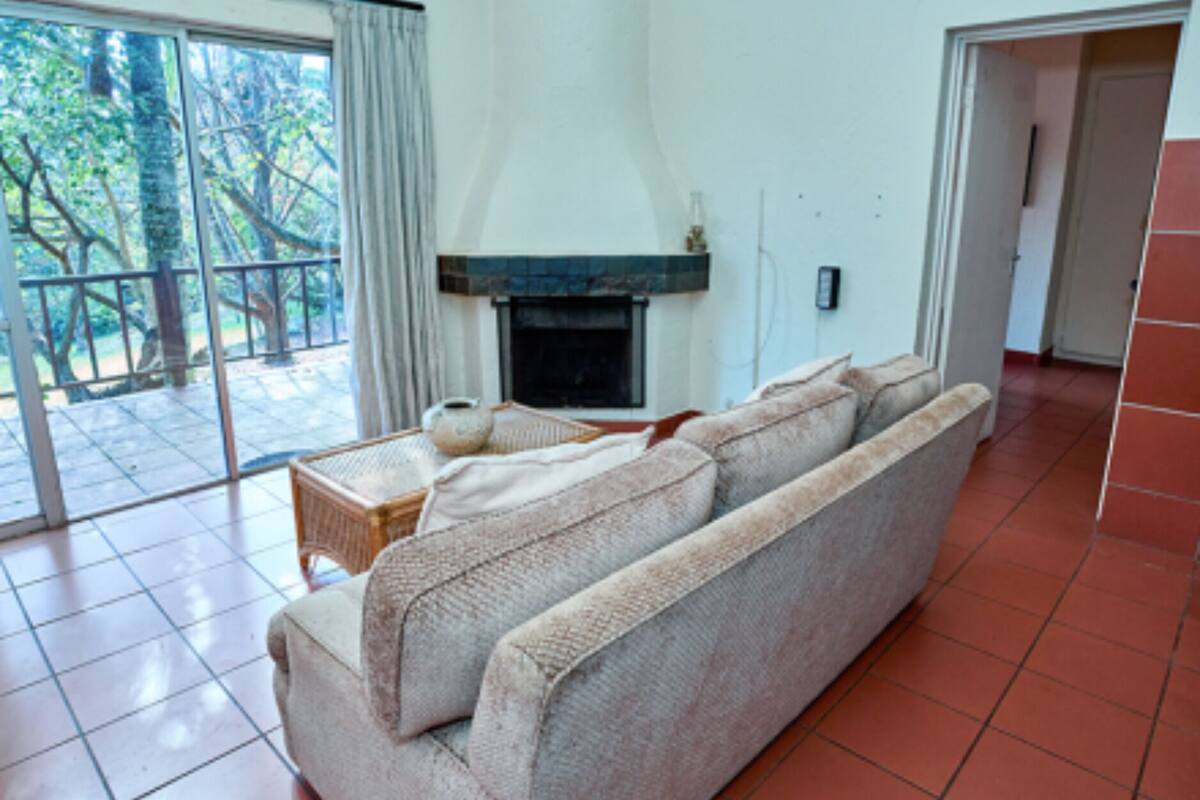 A living room with a sofa, a fireplace, and a view of trees through large windows.