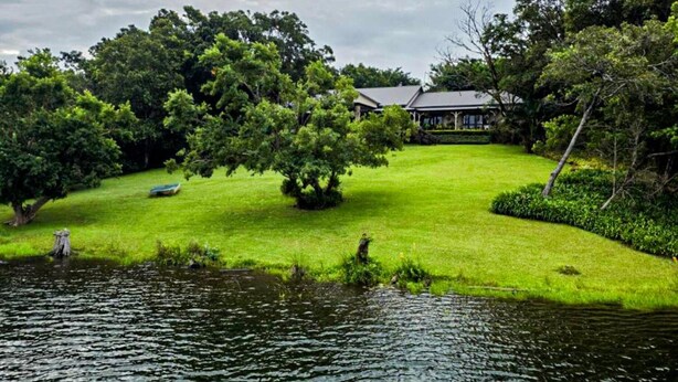 A serene lakeside view with a well-maintained lawn, a gazebo, and a house surrounded by lush greenery. - Kruger Island Resort (White River)
