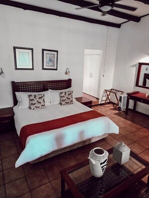 A neatly made bed with a red blanket, a bedside table with a white vase, and a chair with a black and white patterned vase. - Kruger Island Resort (White River)