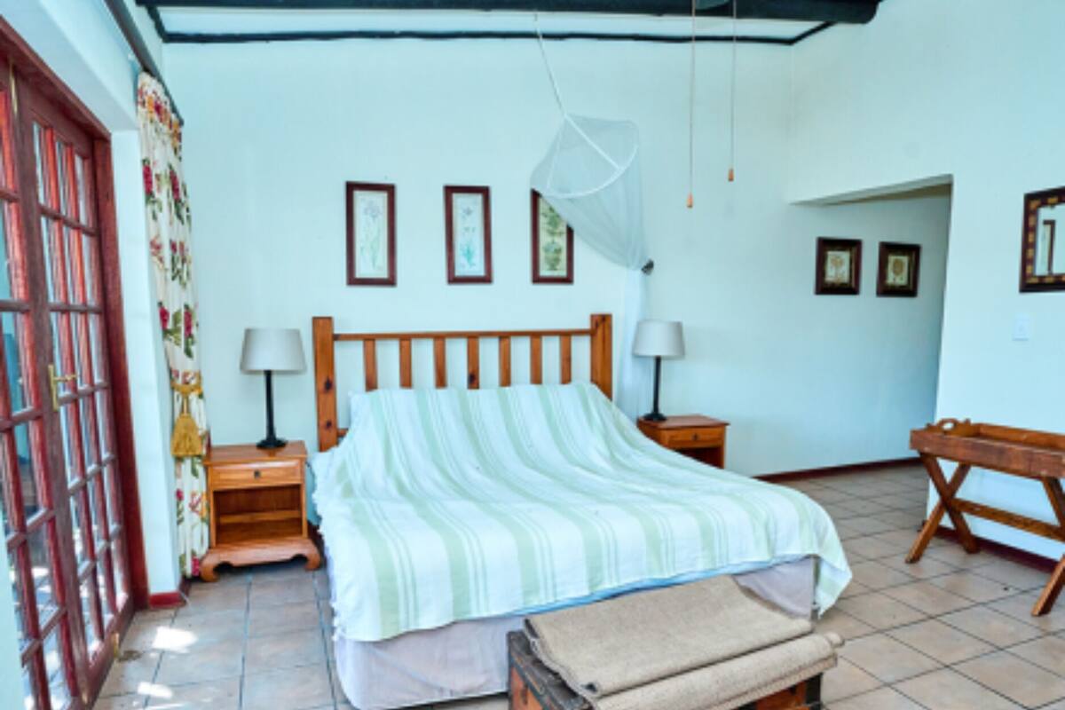 A bedroom with a bed, bedside tables, a wooden bench, and a mosquito net.