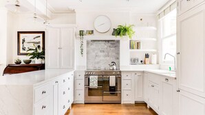 A kitchen with white cabinetry, a marble backsplash, and a wooden floor.