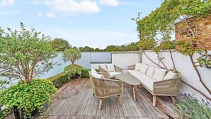 An outdoor patio with wicker furniture, a view of the sky, and greenery.