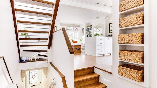 A staircase with wooden steps and a white wall. There are wicker baskets on the wall and a white cabinet in the background.
