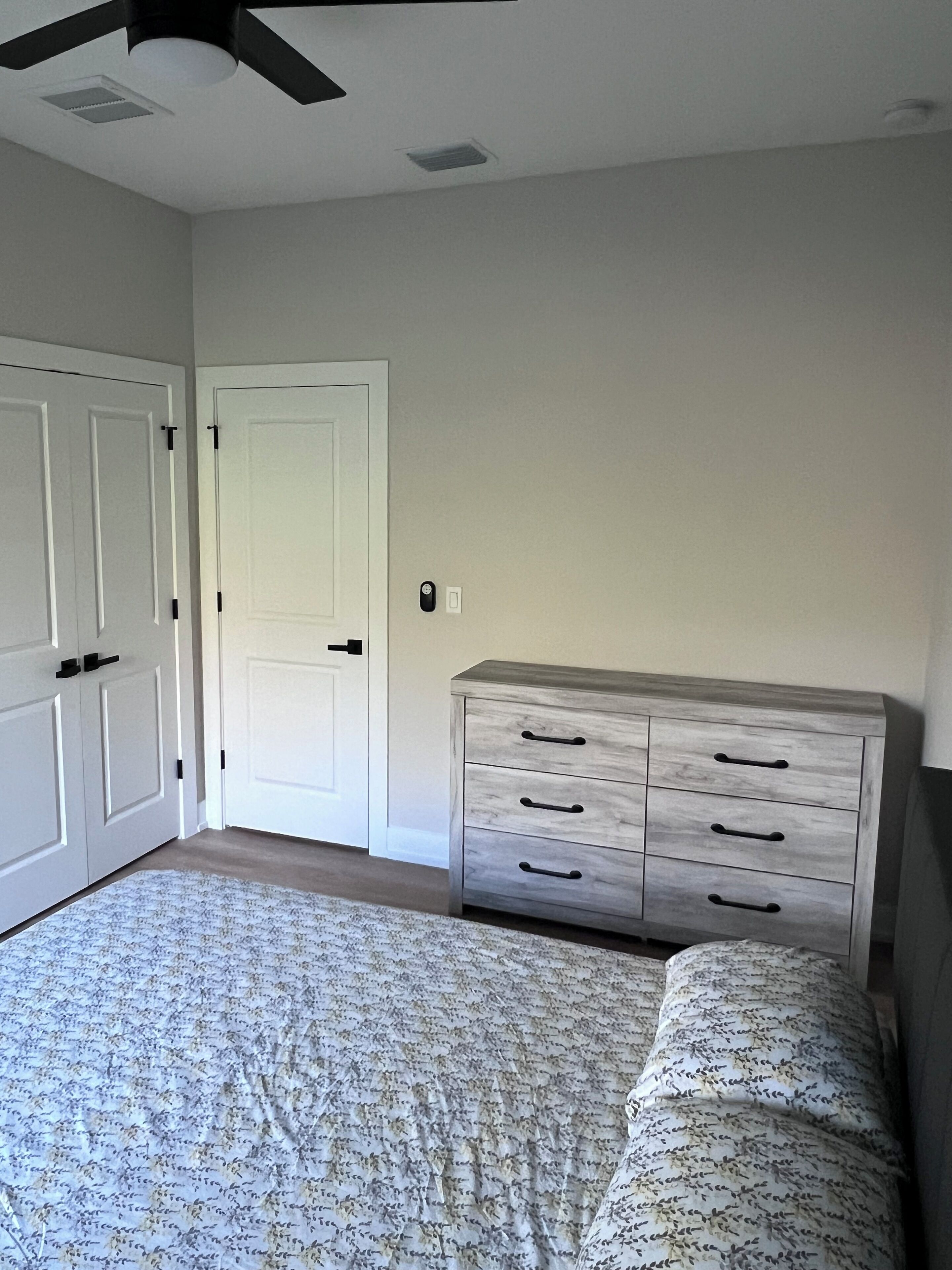 A bedroom with a bed, a dresser, a ceiling fan, and a door.