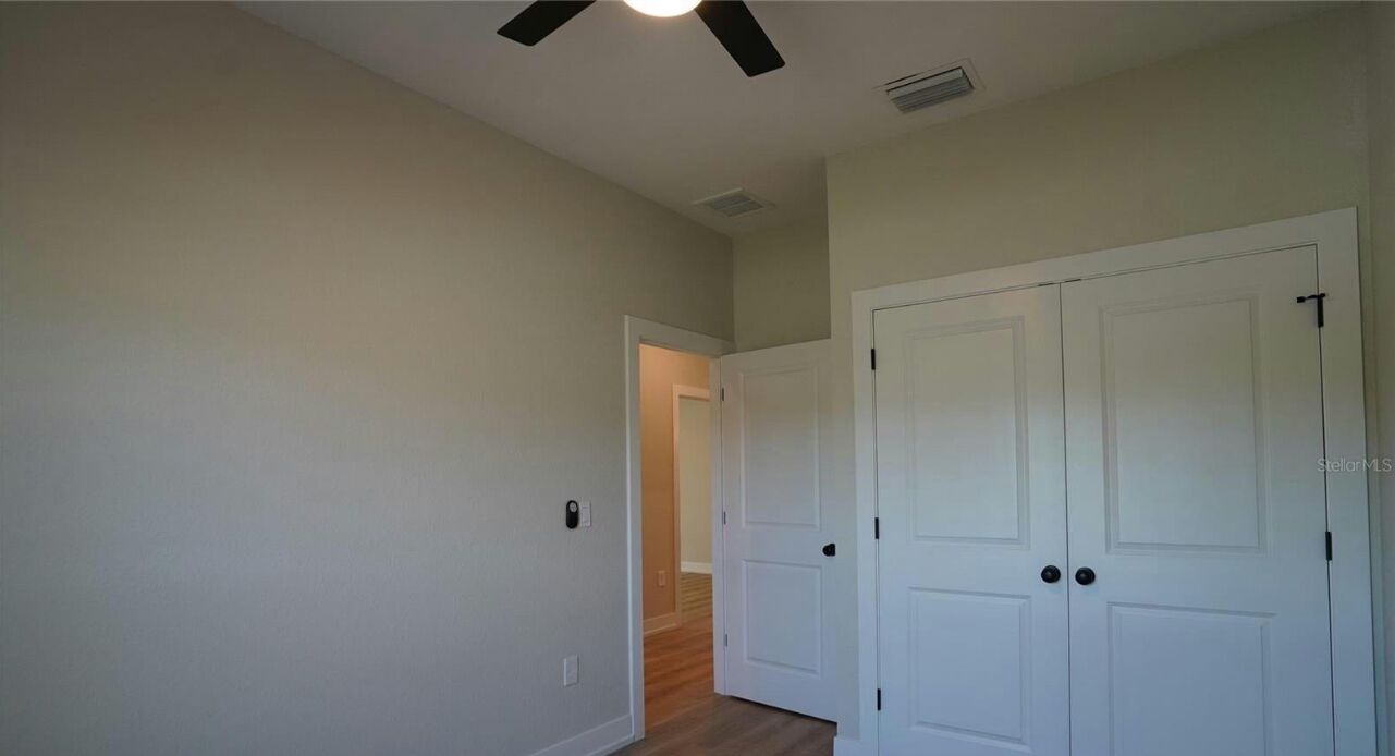 A hallway with white walls, a ceiling fan, and a door leading to another room.