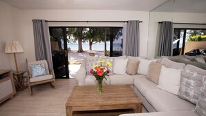 Un salón con un sofá, una mesa de centro y una silla. Se ve el exterior a través de amplios ventanales.