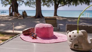 Escena de playa con una silla de mimbre, un sombrero rosa de crochet y una figura de elefante de cerámica sobre una mesa.