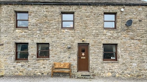 A stone building with four windows, a door, and a bench outside. - 4 Swallowholm Cottage (Arkengarthdale, near Reeth)