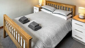 A neatly made bed with a floral bedspread, two pillows, and two folded towels. There are two bedside tables with lamps and a small framed picture on the wall. - 4 Swallowholm Cottage (Arkengarthdale, near Reeth)