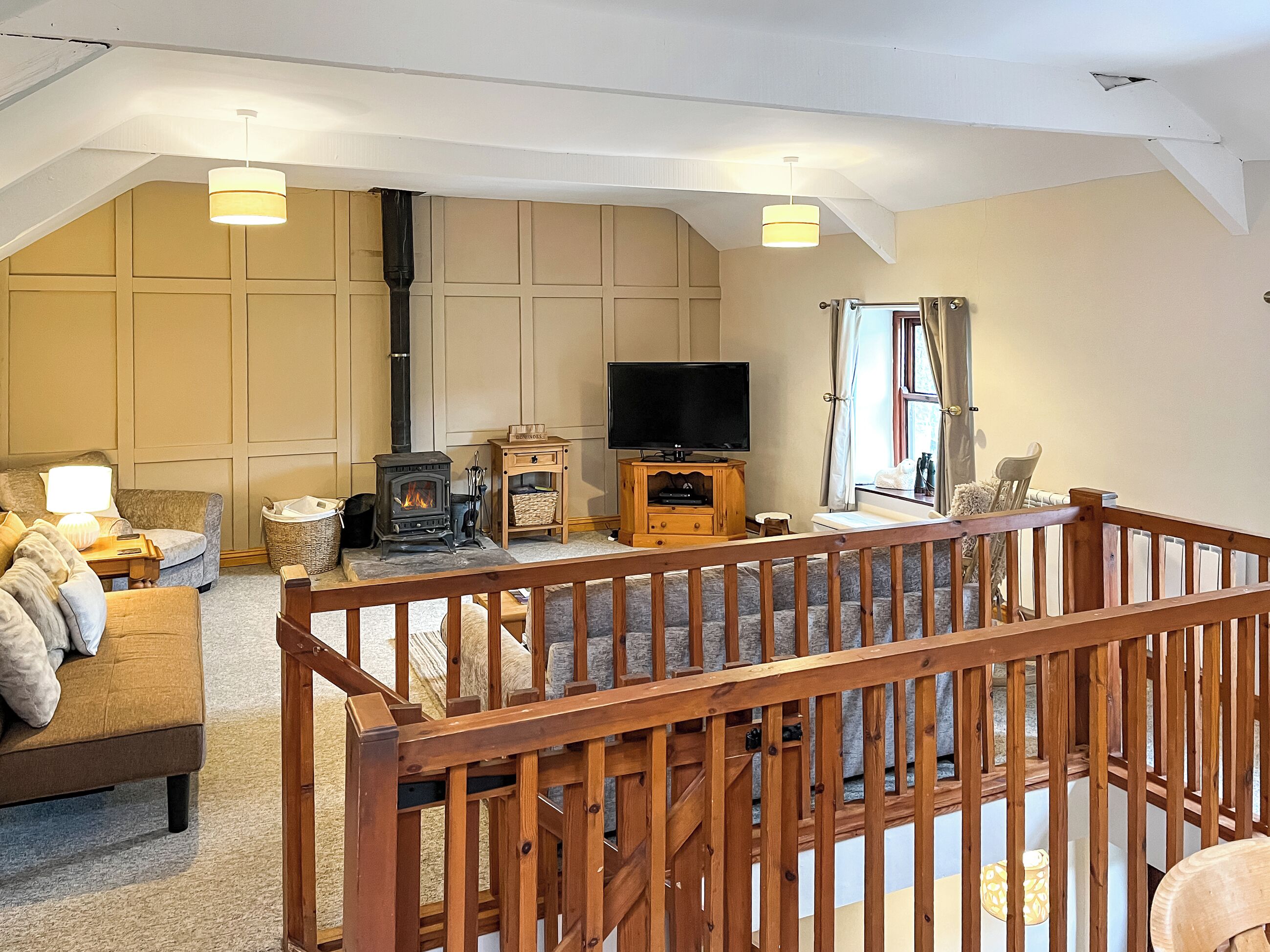 A cozy living room with a fireplace, a television, and a wooden railing.