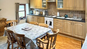 A kitchen with wooden cabinets, a dining table with chairs, a window, and a view of the outdoors. - 4 Swallowholm Cottage (Arkengarthdale, near Reeth)
