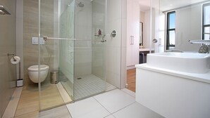 Un baño moderno con ducha envuelta en vidrio, inodoro blanco y una bañera amplia.