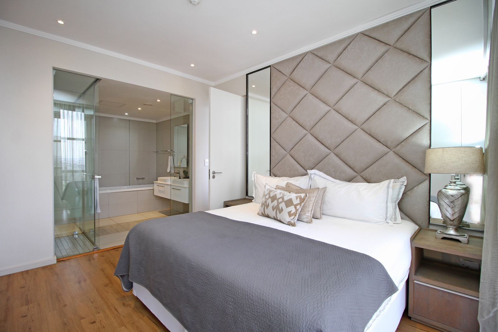 A modern bedroom with a large bed, a glass shower enclosure, and a mirrored headboard.