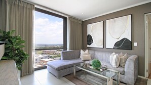 Un salón moderno con un sofá gris, una mesa de centro de cristal y un amplio ventanal con vistas a la ciudad.