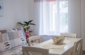 Une table à manger avec un saladier, des chaises blanches, un canapé matelassé et une plante.