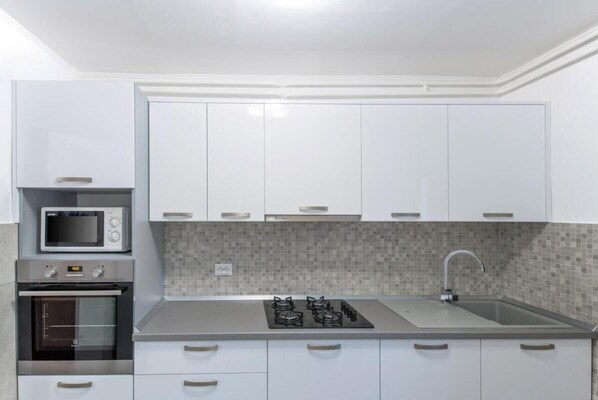 Une cuisine moderne avec des meubles blancs, un four à micro-ondes, un four traditionnel, une cuisinière à gaz et un dosseret carrelé.