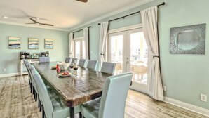 Comedor con una larga mesa, sillas, ventiladores de techo y vistas amplias por las ventanas.