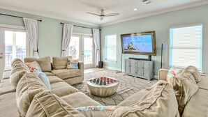 A living room with a beige sofa set, a coffee table, a flat-screen TV, and a ceiling fan.