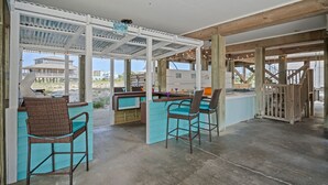 Un área de bar al aire libre con techo, pilares de madera, una piscina y vista a la playa.