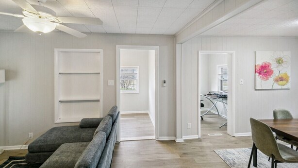 A spacious living room with a gray sectional sofa, a dining table with chairs, and a ceiling fan. - 5 Bed Home w/ Big Yard & Front Porch by Navy Base (Libertyville)