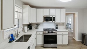 A modern kitchen with white cabinets, stainless steel appliances, and a wooden floor. - 5 Bed Home w/ Big Yard & Front Porch by Navy Base (Libertyville)