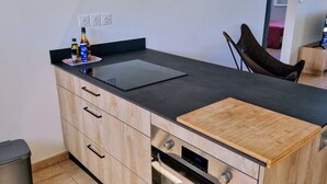 A modern kitchen with a built-in oven, a sink, and a countertop. There are three framed pictures on the wall and a chair in the corner. - Large T3 • Breathtaking ocean view - Saint-Gilles (Saint-Paul)