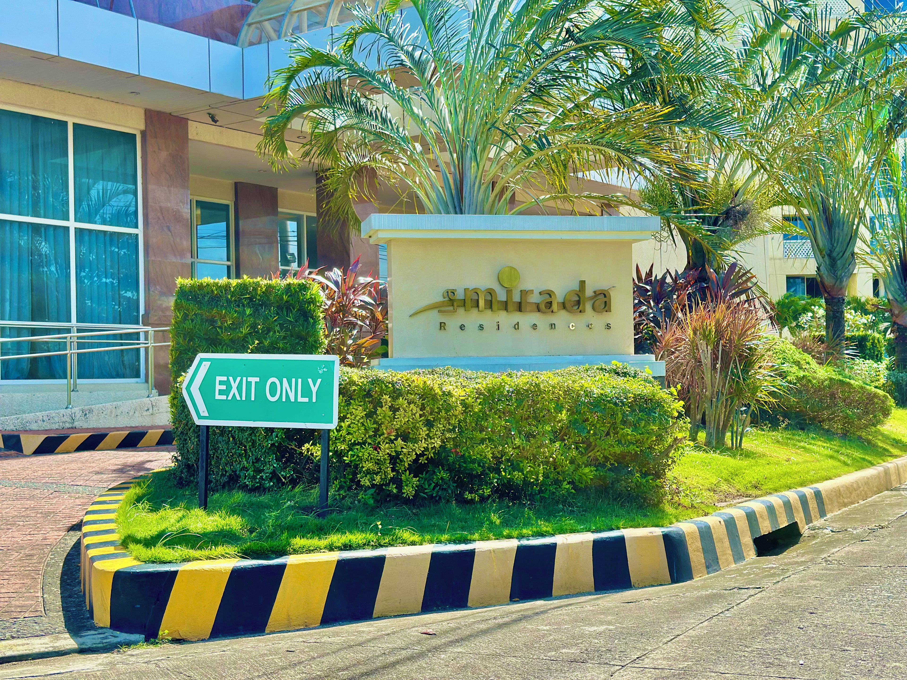 A sign for 'Mirada Residences' with an 'EXIT ONLY' sign, surrounded by greenery and a building facade.