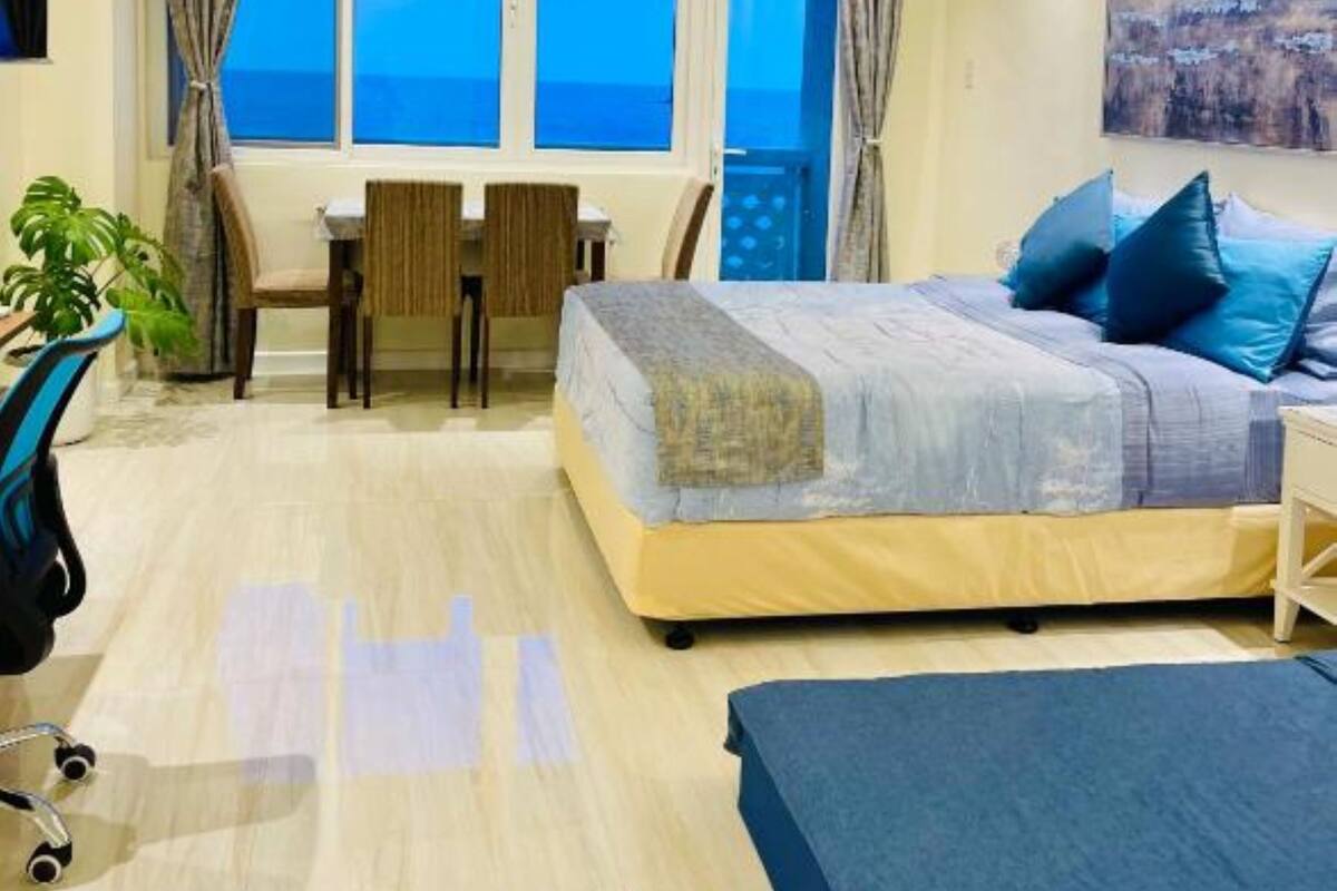 A bedroom with a bed, a desk, and a chair. There is a window with curtains, a plant, and a painting on the wall.