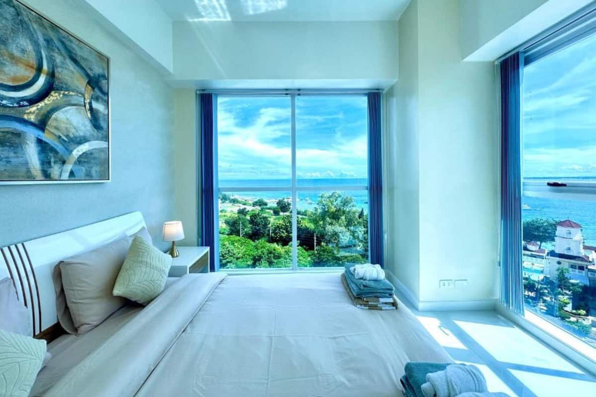 A modern bedroom with a large bed, a view of the sea, and a cityscape.