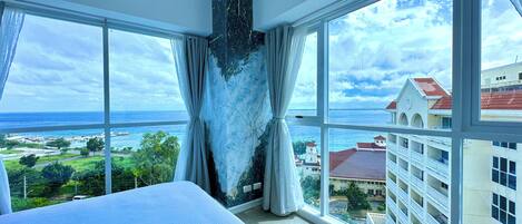 Camera d'albergo con un letto grande, una parete decorata in marmo e vista sull'oceano e sugli edifici.