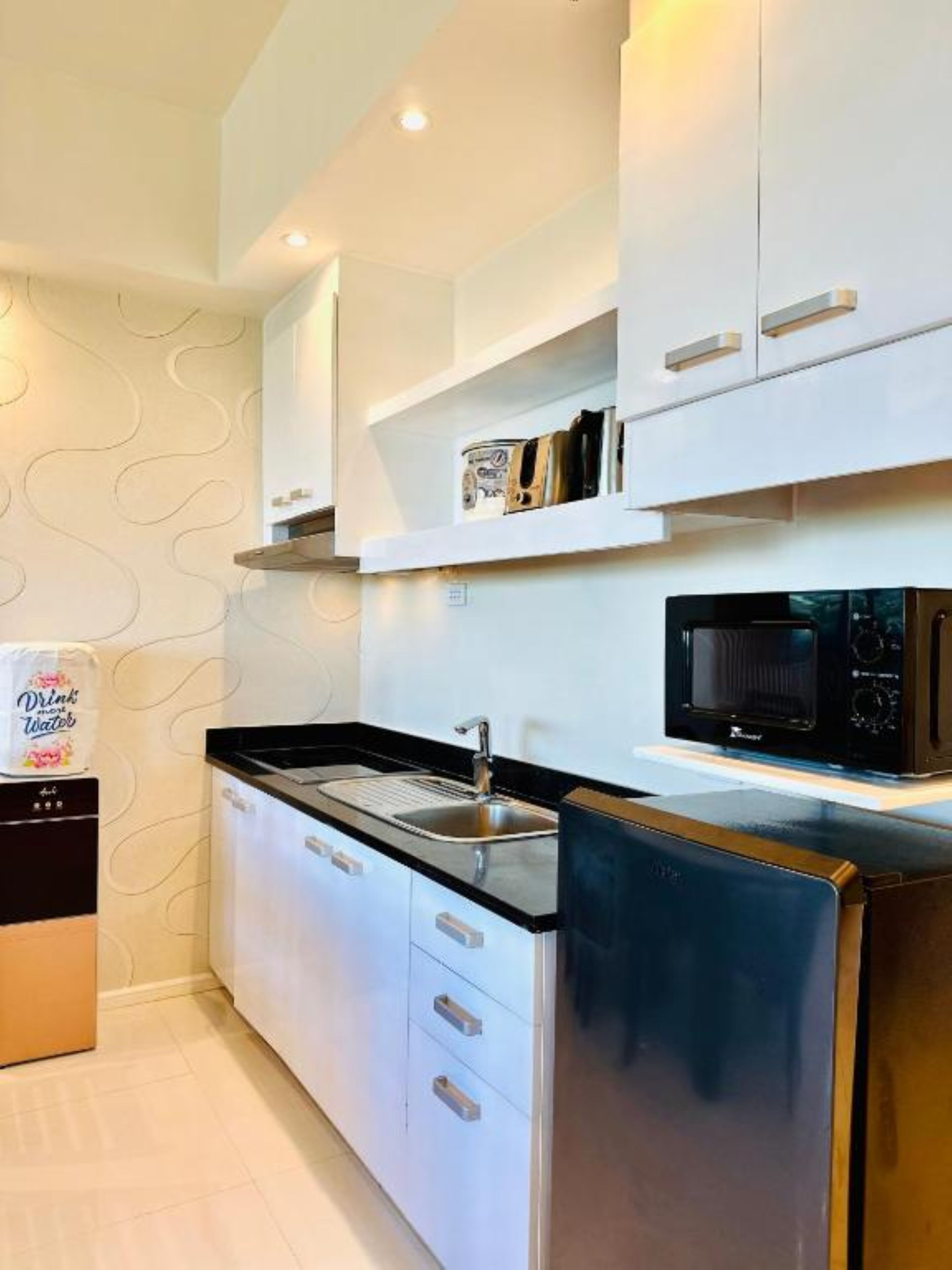 A modern kitchen with white cabinets, a stainless steel refrigerator, and a black microwave.