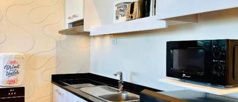 A modern kitchen with white cabinets, a stainless steel refrigerator, and a black microwave.