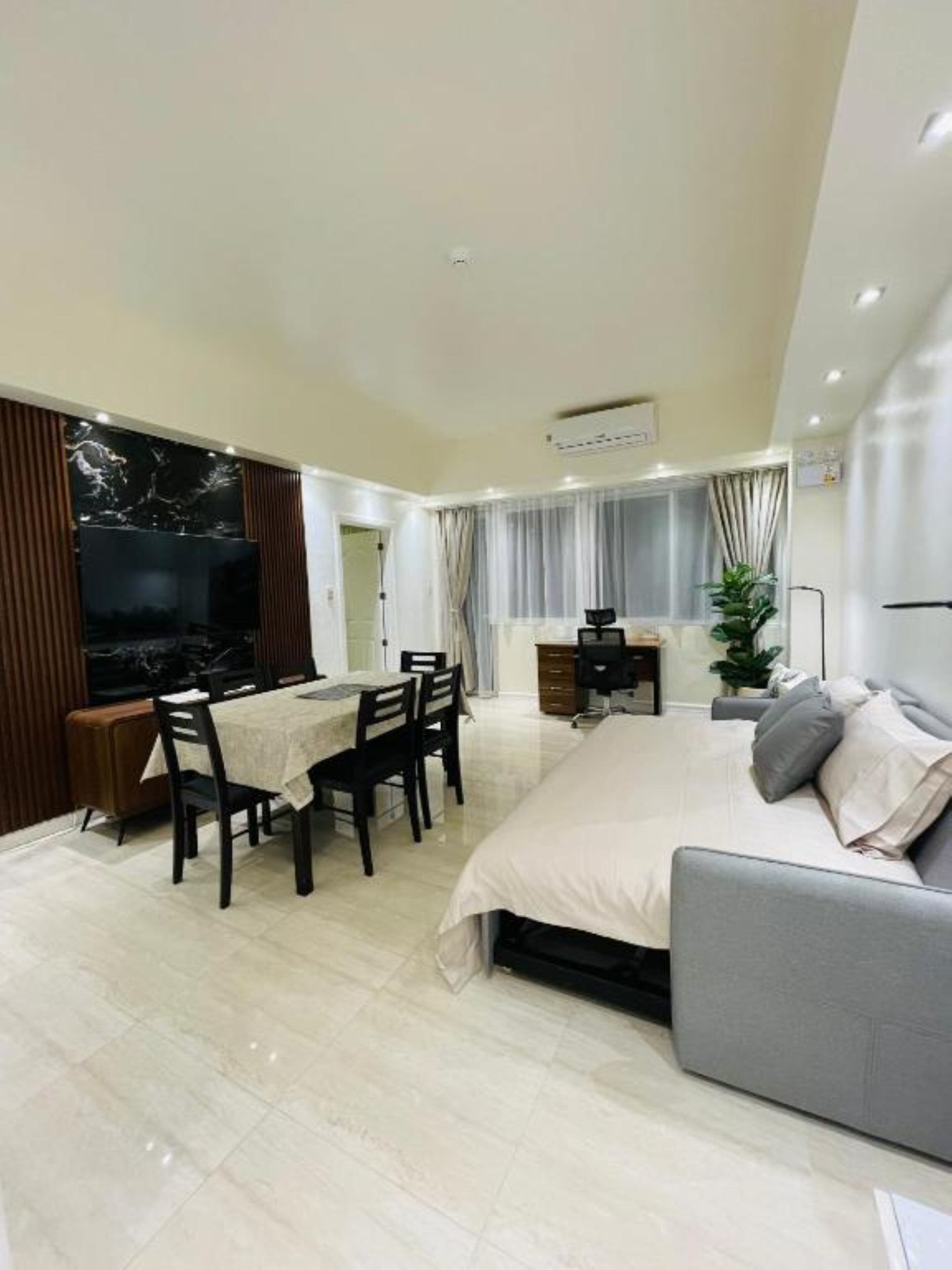 A modern hotel room with a large bed, a dining area, a desk, and a TV.