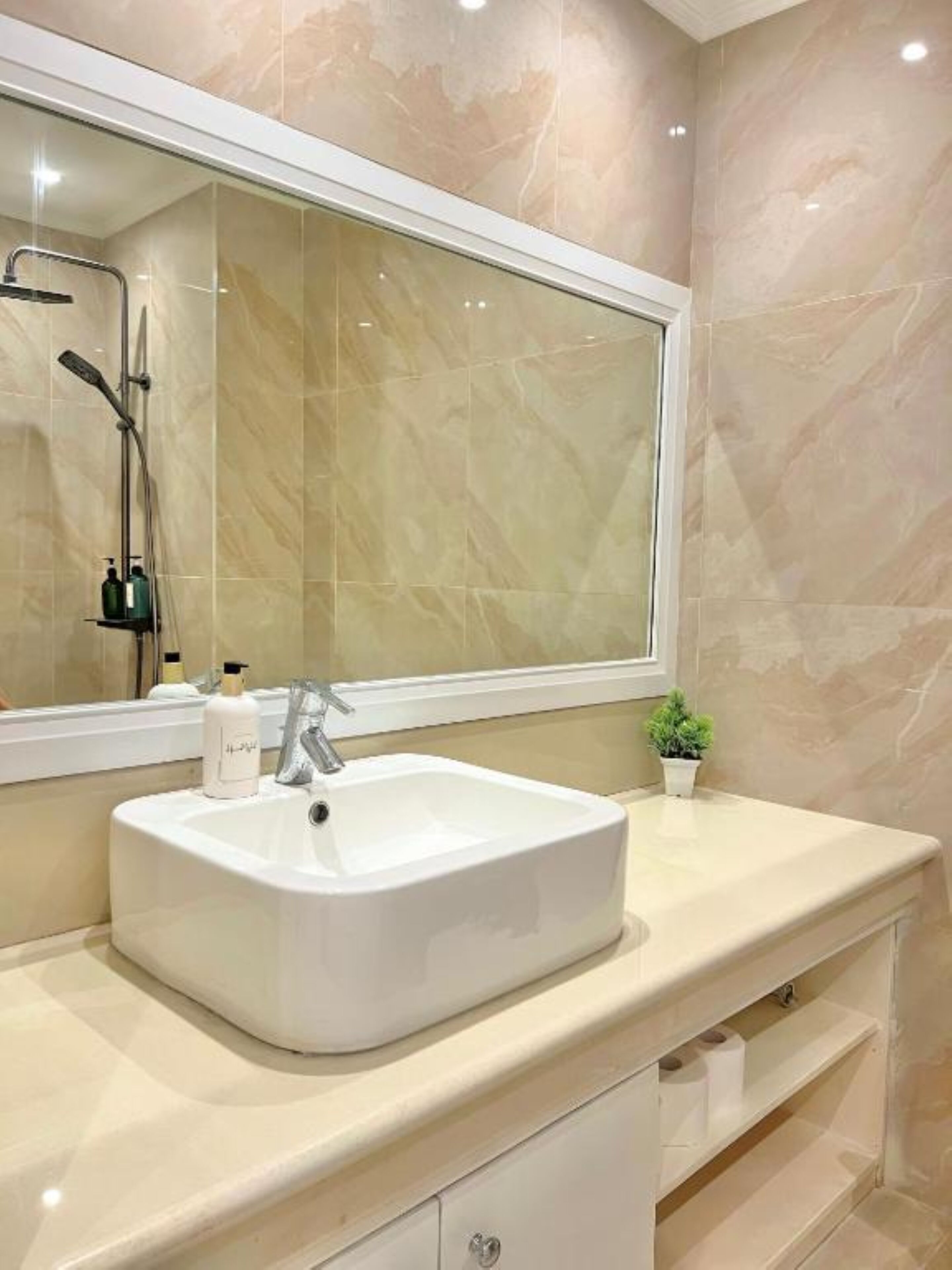 Un baño con un espejo grande, un lavamanos blanco y una ducha.